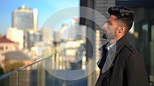 Troubled anxious Middle Eastern man hitting glass fence on rooftop looking away at urban city. Side view portrait of