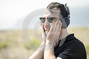 Troubled, attractive man wearing sunglasses and listening to mus