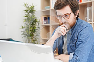Troubled bearded guy feeling doubtful and using laptop