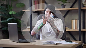 Troubled male tattooed analyst tearing paperwork thinking sitting in home office on Covid-19 pandemic quarantine