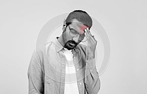 A troubled man with a beard and glasses holds his forehead in a sign of distress or headache