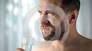 Troubled man drinking water from cup, taking pills, feeling ache, painkillers