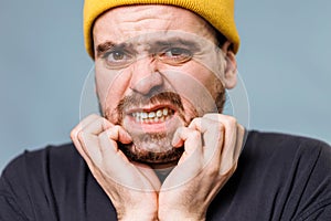 Troubled man looking at camera has beard itch in blue background studio portrait. close up