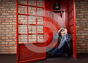 Troubled Man Sitting on Floor of Telephone Booth