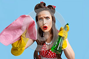 Troubled pin up woman in retro dress cleaning screen with detergent and rag, wearing rubber gloves on blue background