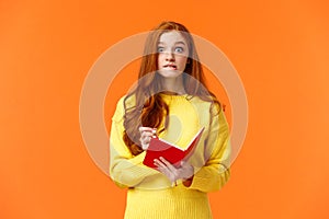 Troubled redhead caucasian girl forgot about appointment, remember task after looking notebook, biting lip and stare