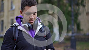 Troubled thoughtful African American young man with smartphone standing at university campus looking around talking