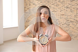 Troubled woman with alarm clock indoors. Time management concept