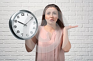 Troubled woman with clock against white brick wall. Time management concept