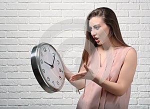 Troubled woman with clock against white brick wall. Time management concept