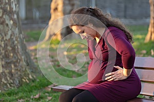 Troubled young pregnant woman on a park bench
