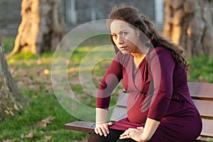 Troubled young pregnant woman on a park bench