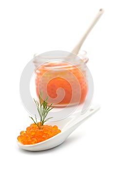 Trout roe in a ceramic spoon with a dill leaf with a transparent glass container on white background