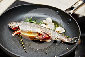 trout stuffed with lemon and tomato in a frying pan with rosemary