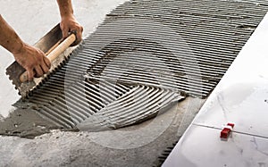 Troweling mortar onto a concrete floor in preparation for laying white floor tile