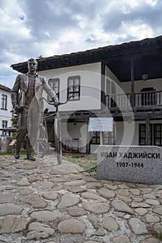 TROYAN, BULGARIA - March 2, 2020:StatuÐµ of man with bycicle in front of traditional Bulgarian house near the Museum of Folk Arts