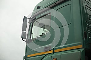 Truck cab on side. Green truck body. Transport details. Rear-view mirror of car