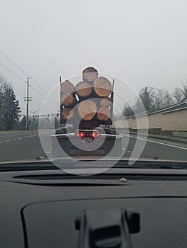 A truck carrying large wood logs driving ahead looking out the windshield on the freeway