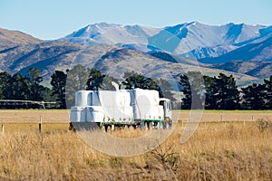 A truck delivers wrapped bales of stock food to a farm on a rural New Zealand road