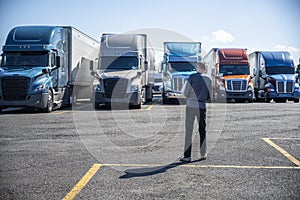 Truck driver carries a shopping box in his hands and going to his big rig semi ruck parked on the truck stop parking lot