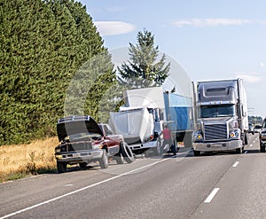 Truck driver changes punctured wheel of the big rig semi truck on the shoulder side of highway next to trucks and cars passing by