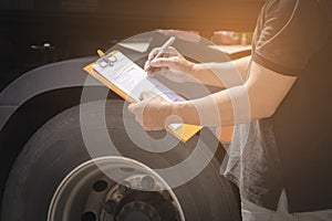 Truck driver holding clipboard his inspecting daily checklist safety of a truck wheels and tires. truck inspection and maintenance