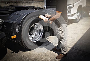 Truck driver holding clipboard his inspecting daily checklist safety of a truck wheels and tires.