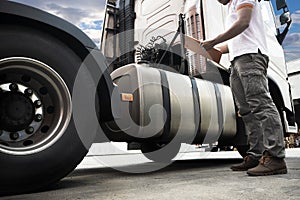 Truck driver holding clipboard inspecting safety fuel tank semi truck