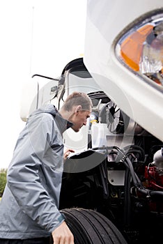 Truck driver inspecting white big rig semi truck engine