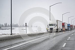 Truck driver is installing chains on semi truck standing on highway road shoulder side in a convoy of big rigs semi trucks with