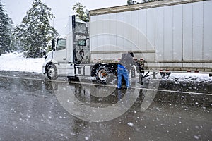 Truck driver puts chains on the wheels of the big rig semi truck with semi trailer to drive safely on a winter highway during a