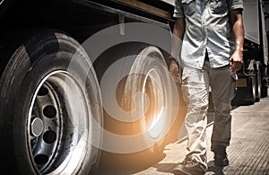 A truck driver walking around a truck, his is checking safety a truck trailer.