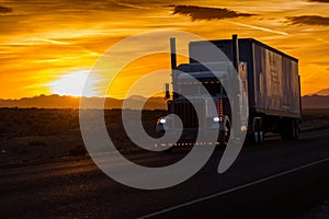 Truck driving along the highway next to a countryside field with the sun setting in the background