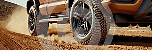 truck is driving on a dirt road with a lot of dust. The tires are black and the truck is leaving a trail of dust behind