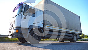 Truck driving on a highway. Lorry rides through the countryside with sunset at background. Bottom Side view Slow motion