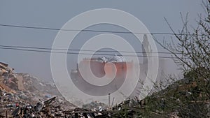 A truck with garbage drives through a landfill. Dust rises into the air. Ecological problems