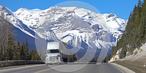 Truck hauls cargo down the highway leading towards snow capped mountains.