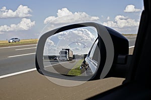 Truck on a highway seen in the rear view mirror on a summer day