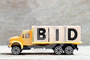 Truck hold block in word bid on wood background photo