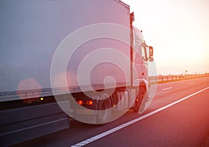 A truck with an isotherm semitrailer transports cargo along the highway against the backdrop of an evening sunset