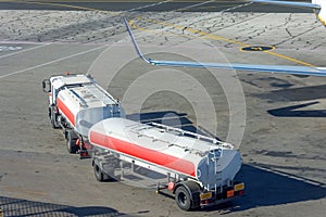 A truck with jet fuel tanks and a trailer on the airfield delivers fuel to the aircraft
