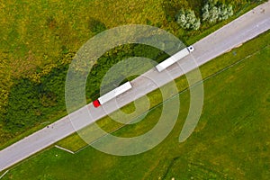 Truck logistic aerial. Two trucks motion by the road between fields. View from drone