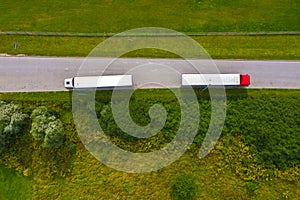Truck logistic aerial. Two trucks motion by the road between fields. View from drone