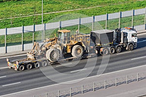 Truck with a long trailer platform for transporting heavy machinery, loaded big tractor with bucket. Highway