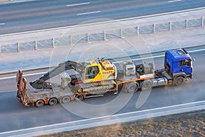Truck with a long trailer platform for transporting heavy machinery, loaded crawler excavator with bucket. Highway transportation