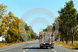 The truck or lorry is moving on the country road with wooden pallet