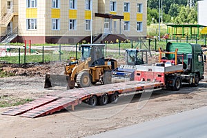 Truck with low loader, road roller and wheeled tractor on road repair