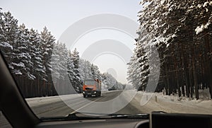 A truck is moving along an asphalt highway. Snow-covered trees grow on the roadsides.