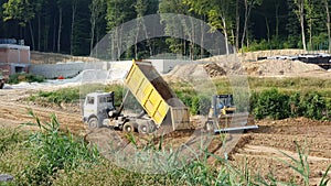 The truck pours sand on the site. Excavator scooping sand bucket.