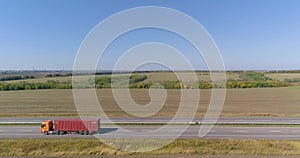 A truck with a red container is driving along the road. A truck with an orange cabin transports a red container view